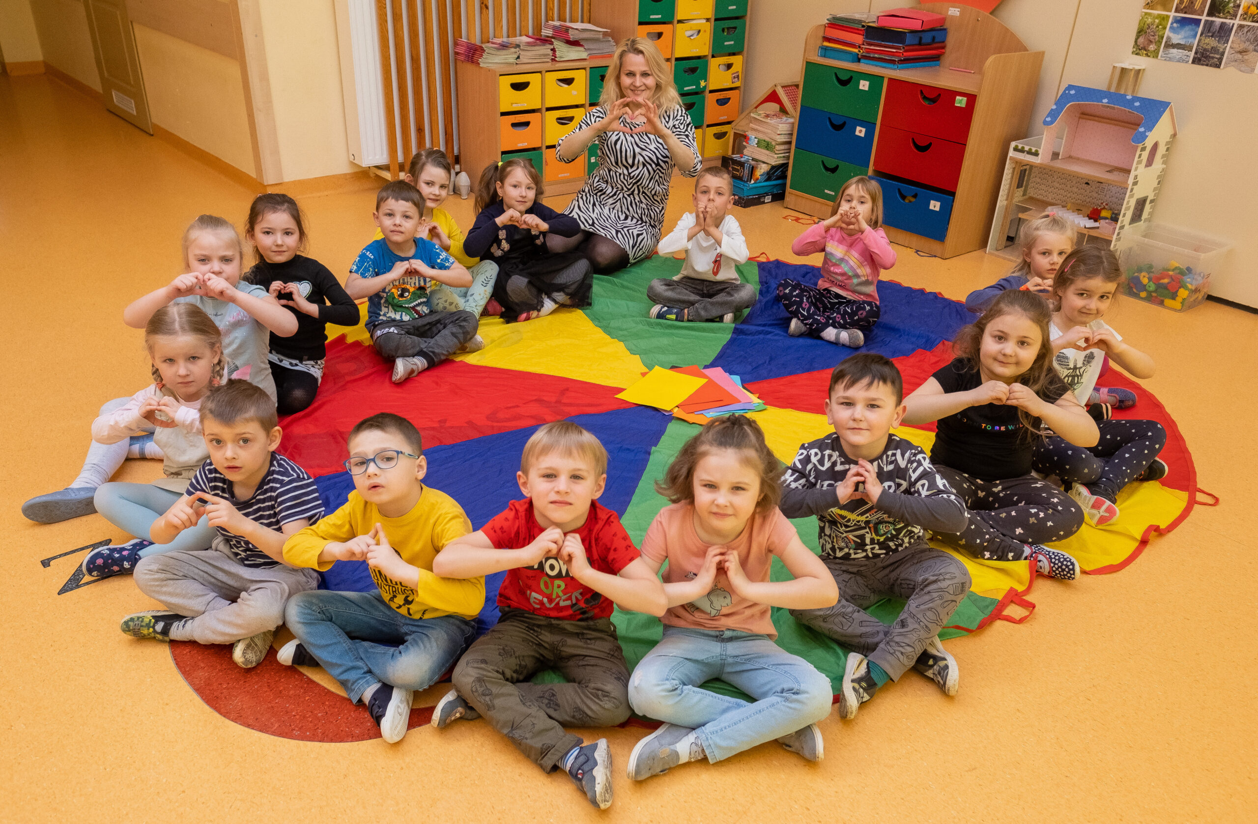 Przedszkolaki siedzące na kolorowej chuście animacyjnej pod opieką Beaty Szwed-Błońskiej